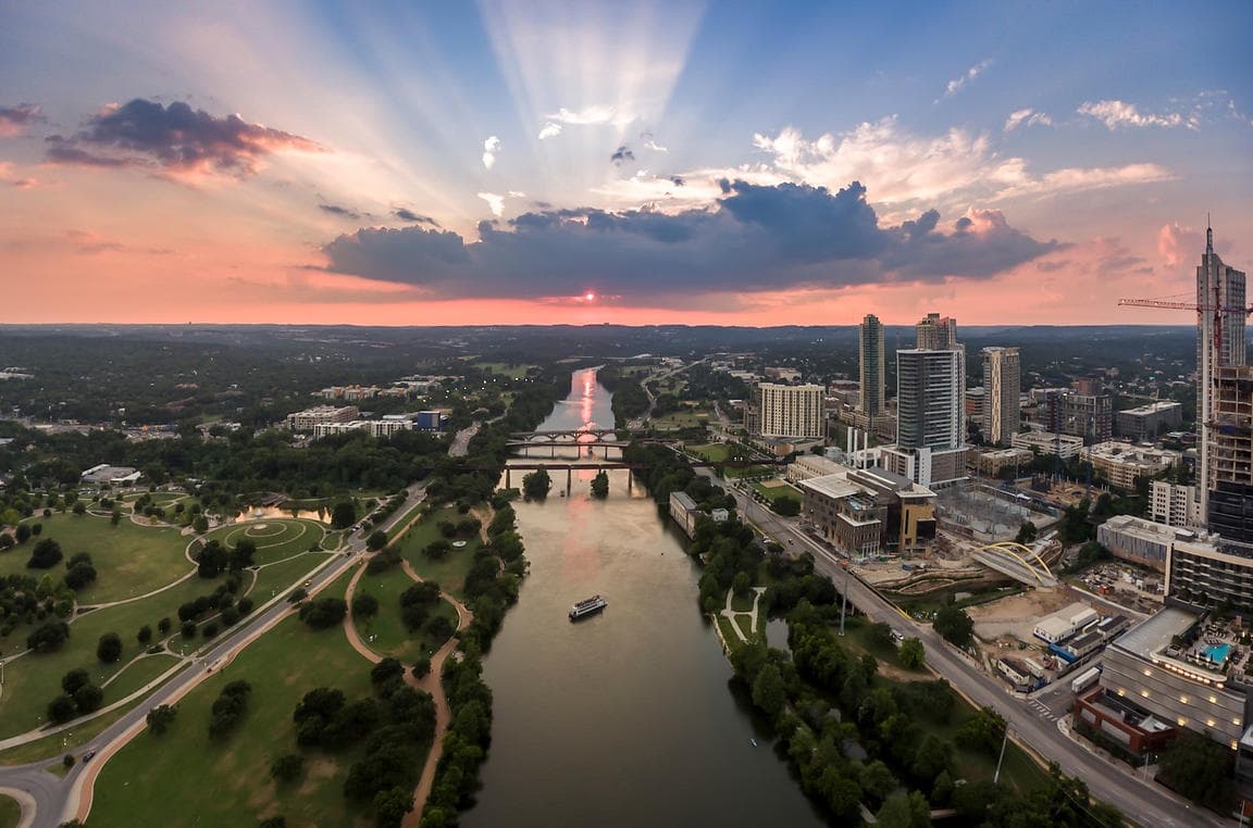 Aerial river and park at sunset with sun rays over city