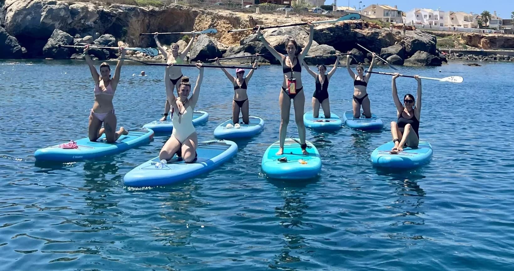 Group stand-up paddleboarders celebrating near rocky coastline
