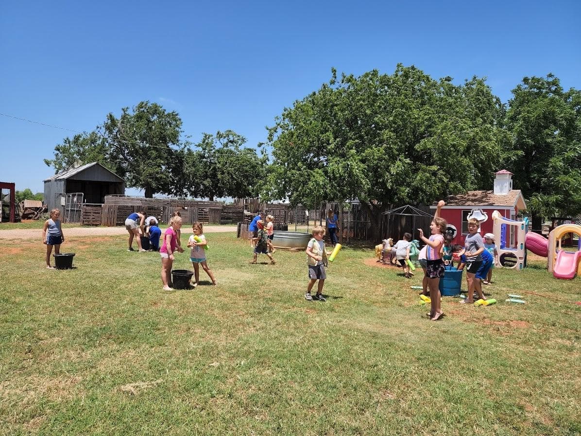 Children playing outdoor games on grassy farmyard with trees