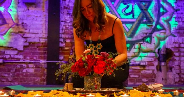 Woman arranging floral altar indoors against graffiti brick wall
