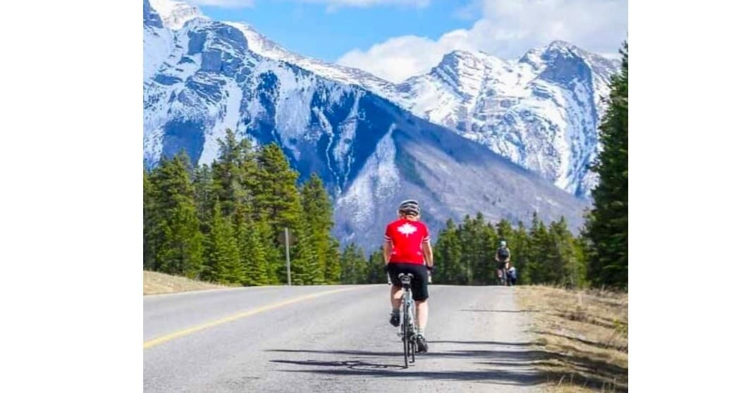 Road cyclist riding toward snowy mountain peaks, scenic road tour