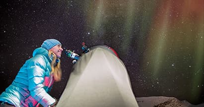 Camper watching vivid aurora beside tent in Jasper backcountry