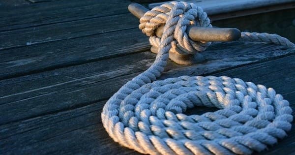 Coiled dock rope tied to cleat on wooden pier at marina