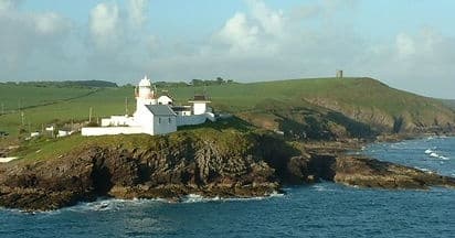 Boat tour past lighthouse on rocky coastal headland