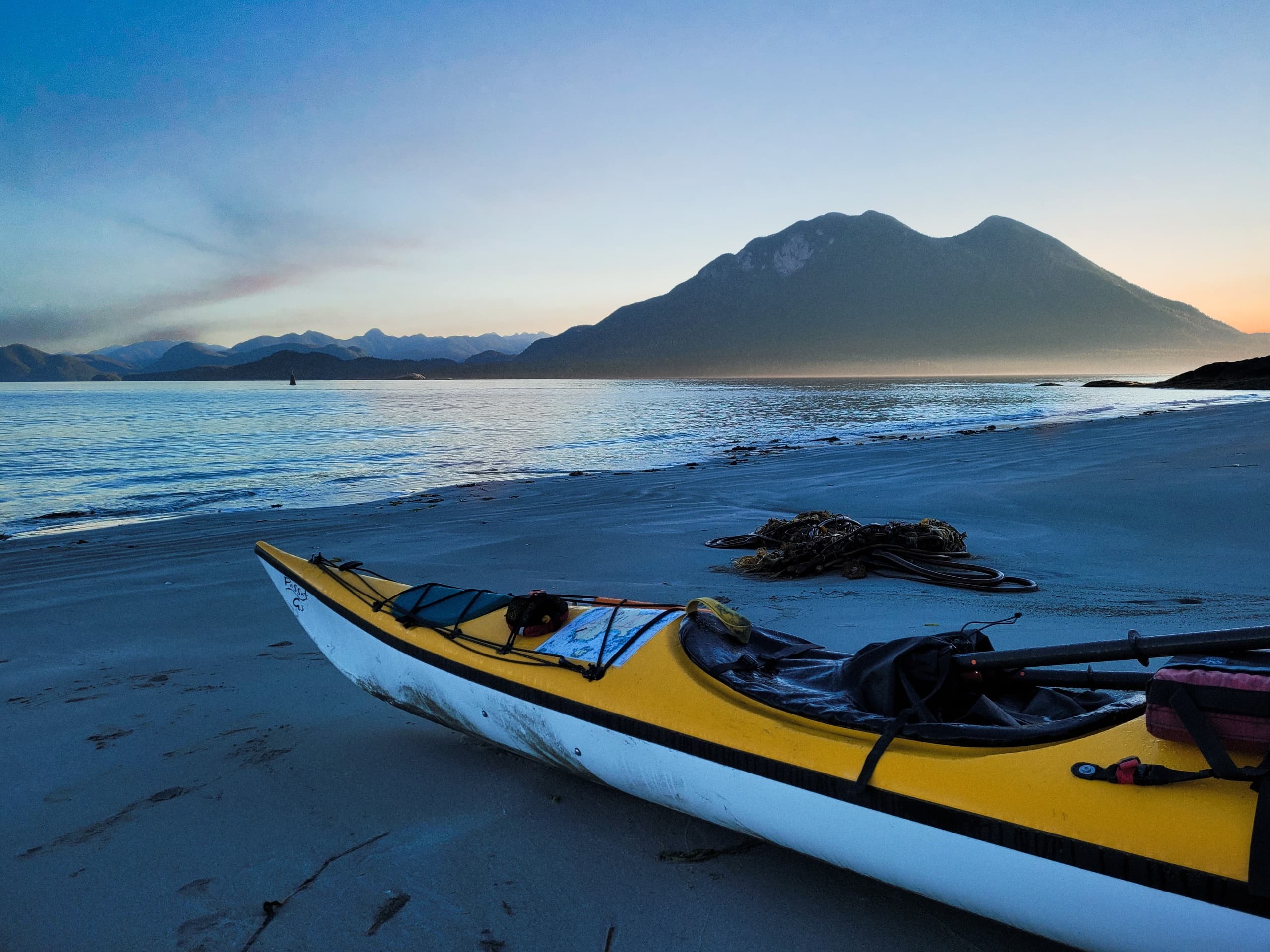 Sea kayak on sandy beach at sunset with mountain backdrop