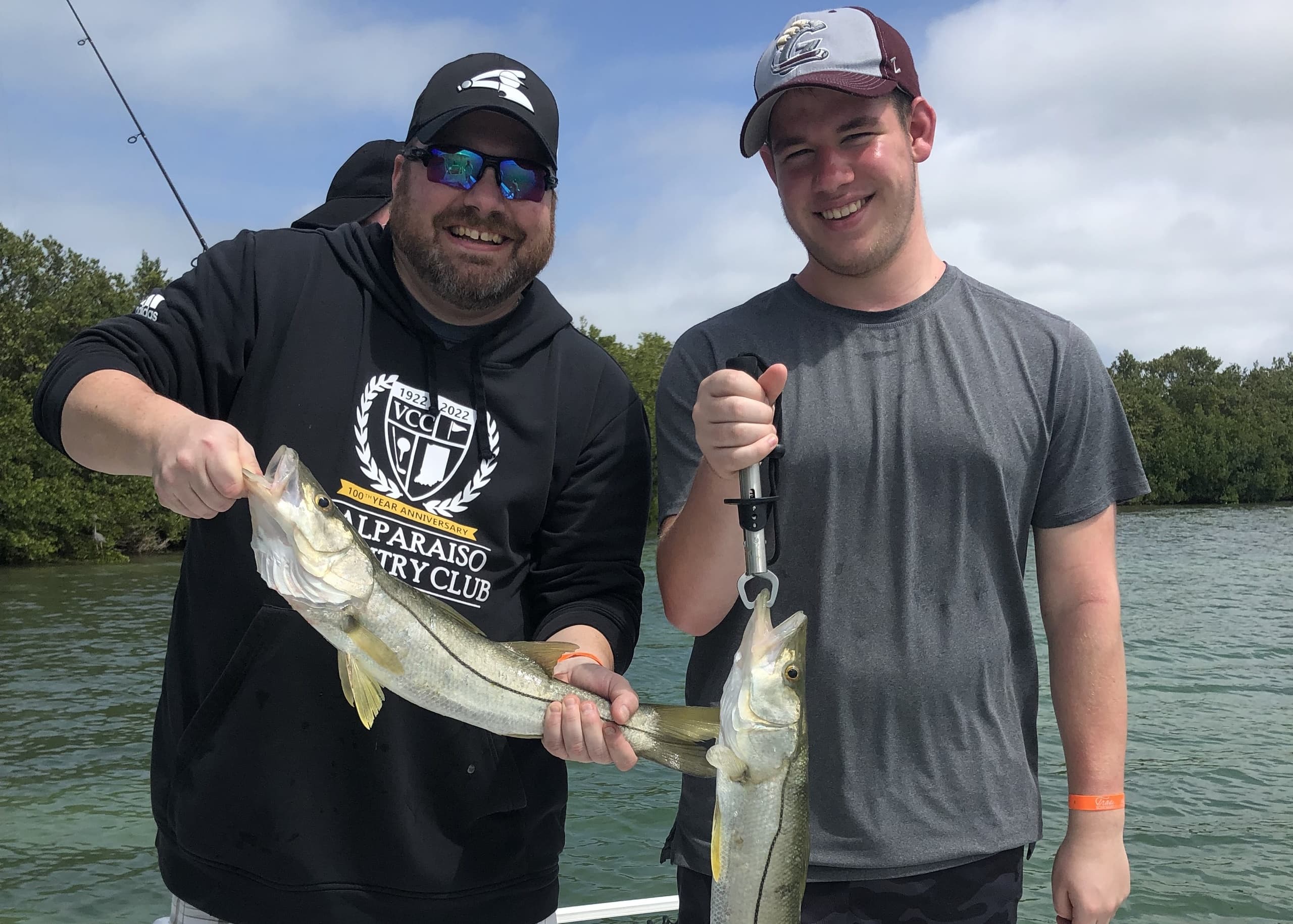 Two anglers holding twin catch with riverine estuary backdrop