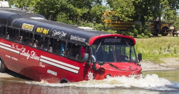 Red amphibious tour bus splashing into river on scenic shoreline