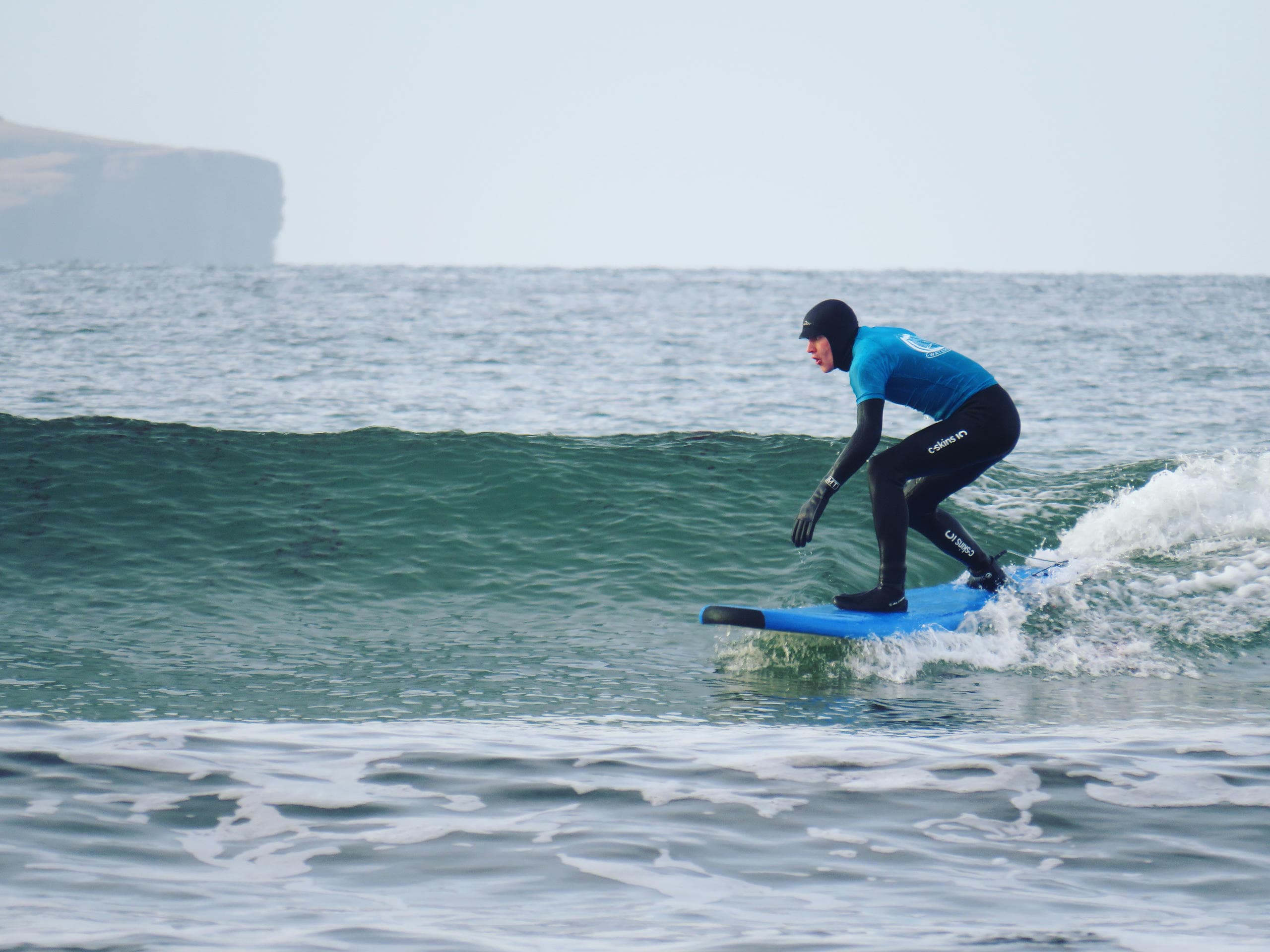 Wetsuit surfer balancing on small green wave in open sea