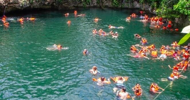Swimmers snorkeling and swimming in turquoise jungle cenote pool