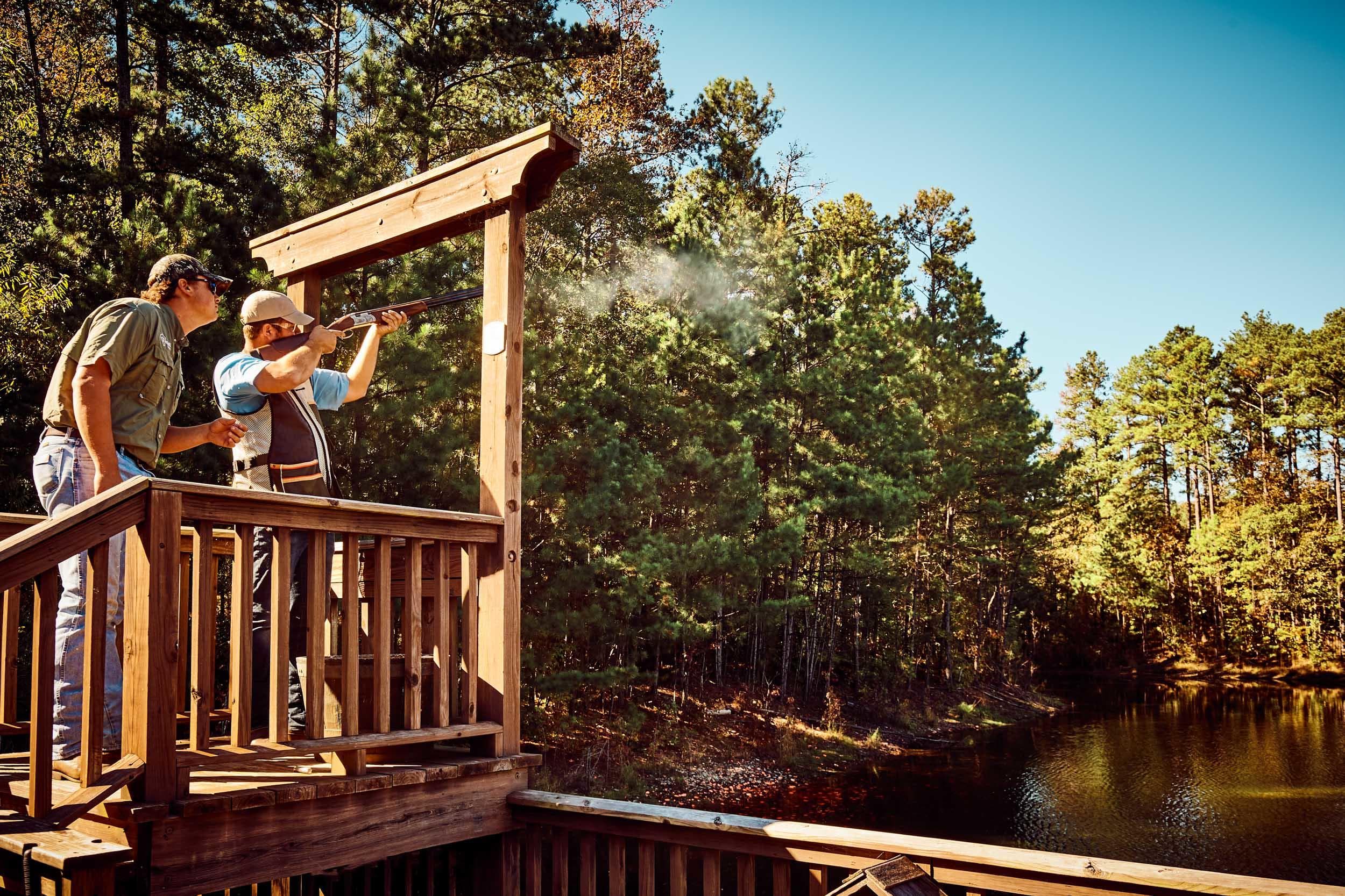 Shooters practicing sporting clays from lakeside wooden platform