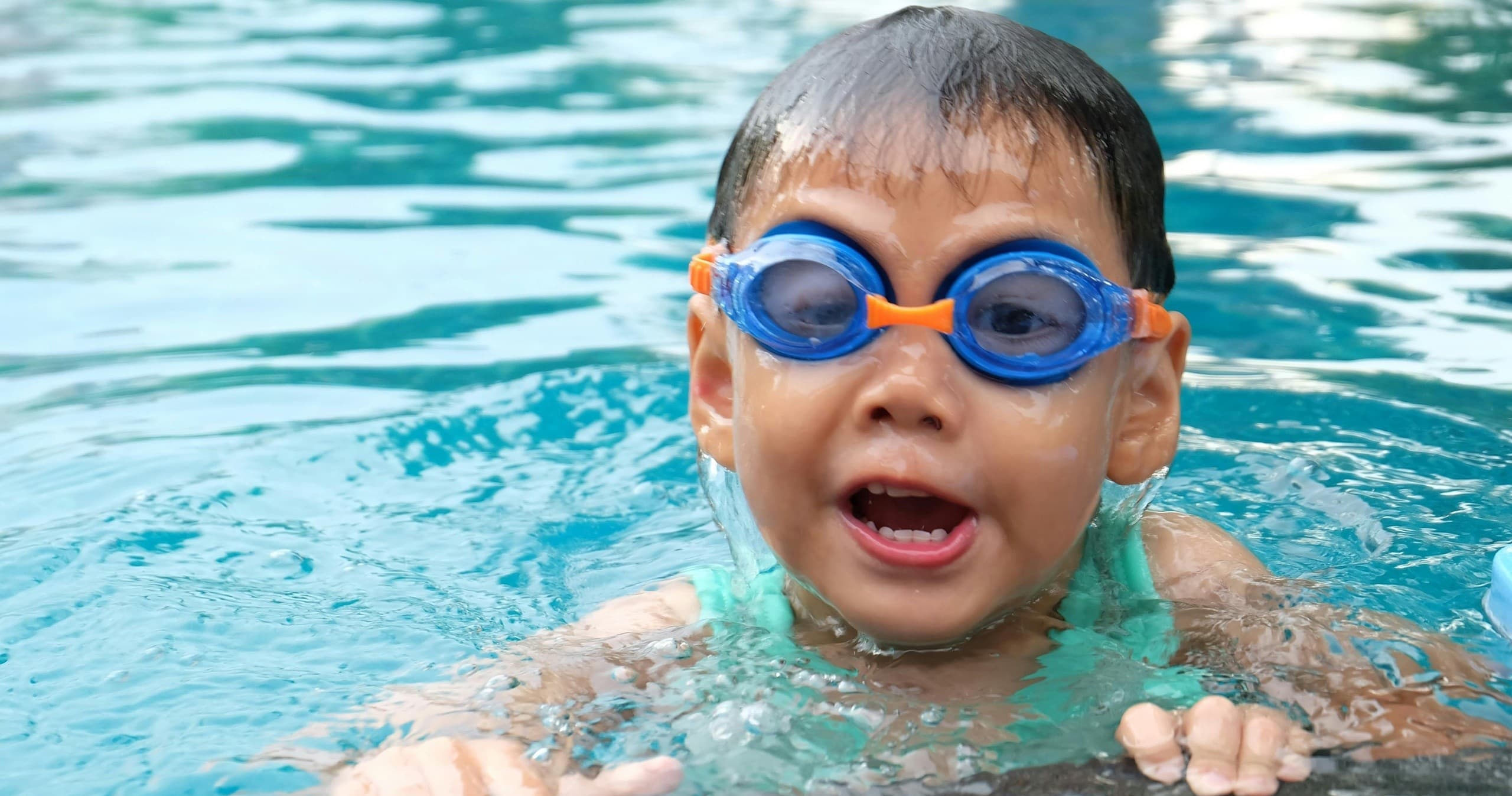 Young swimmer wearing goggles in outdoor pool learning to swim