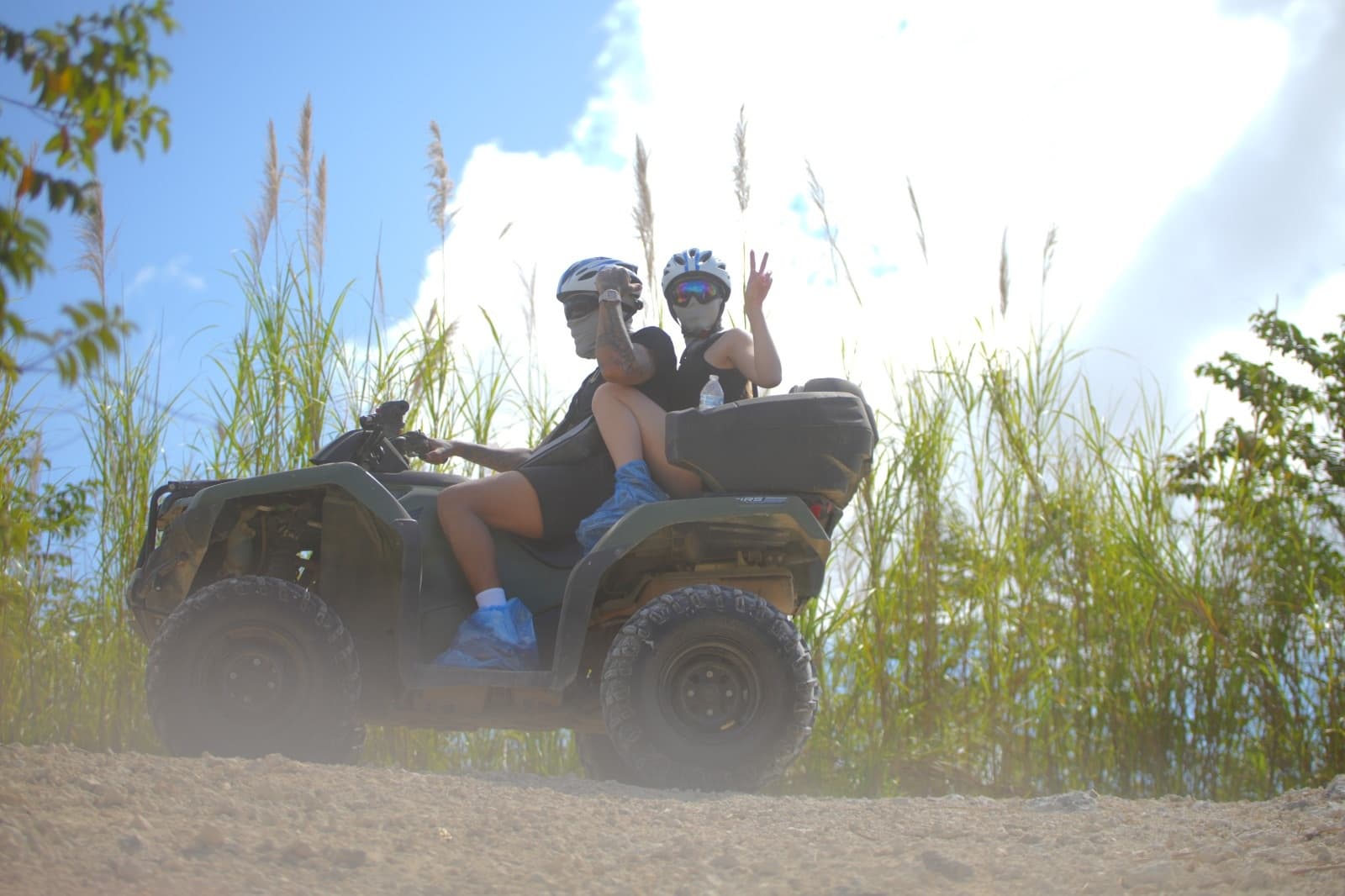 Two ATV riders cruising on sandy trail with tall grasses