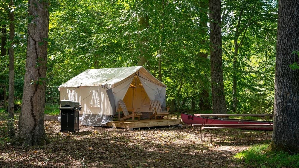 Canvas tent camping with canoe under lush forest canopy