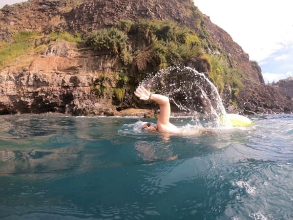 Open-water swimmer splashing near coastal cliffs in Madeira