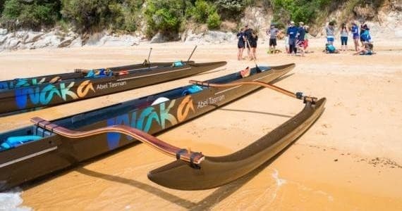 Multiple waka outriggers lined on Abel Tasman sandy beach