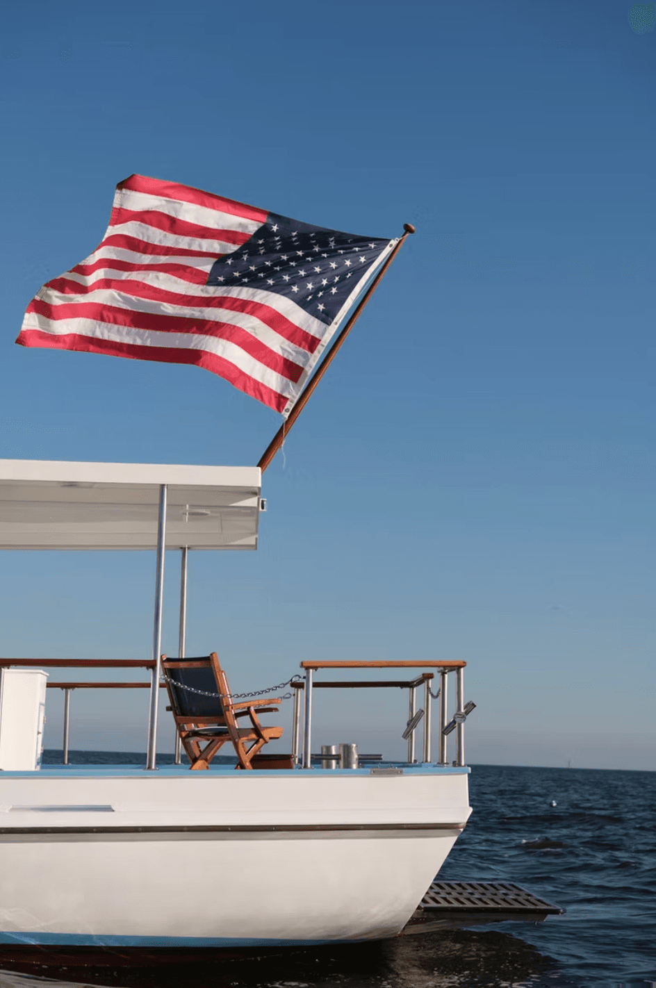 American flag flying from yacht deck over calm coastal waters