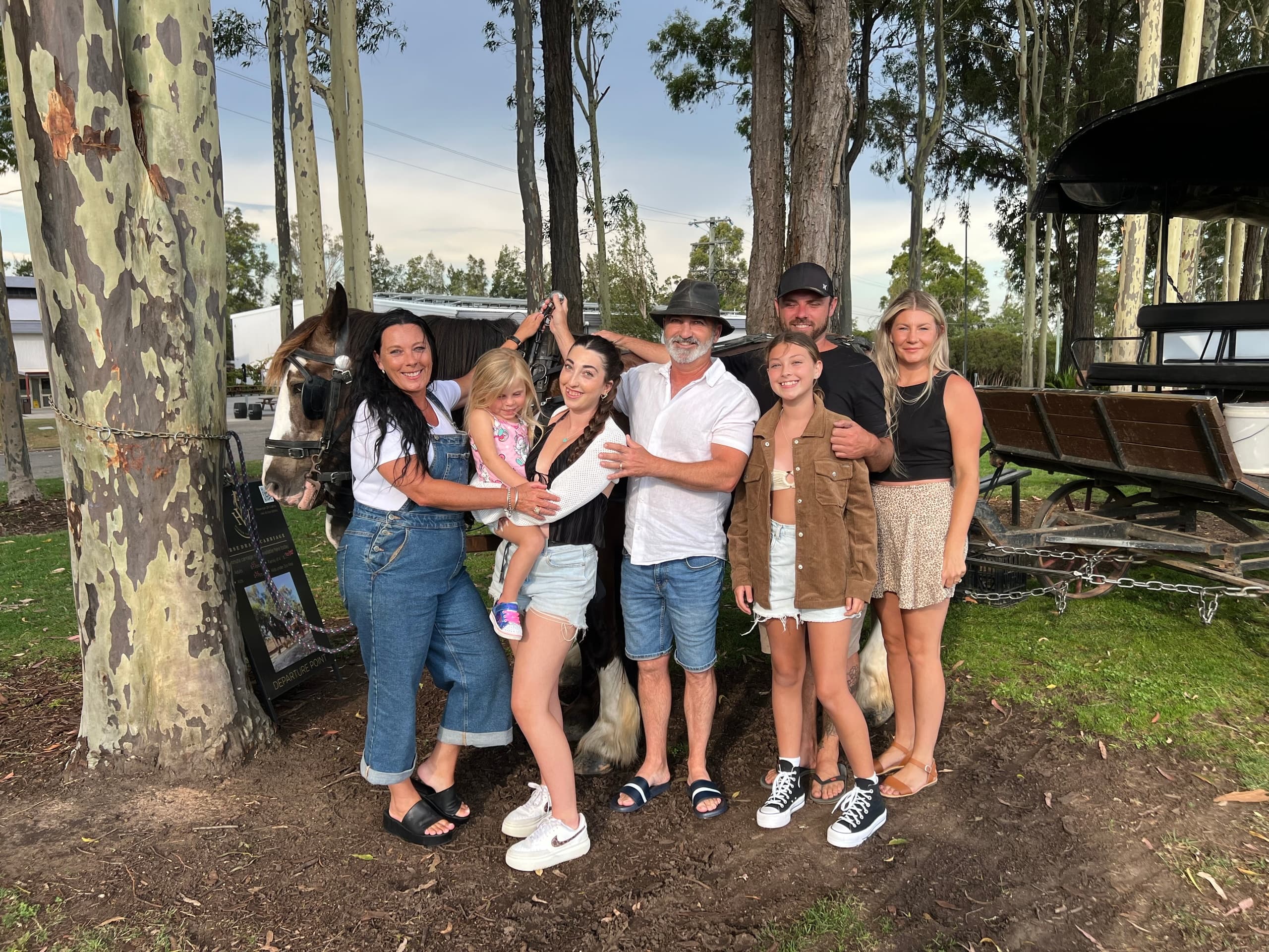 Family posing with horses among eucalyptus trees on rural farm tour