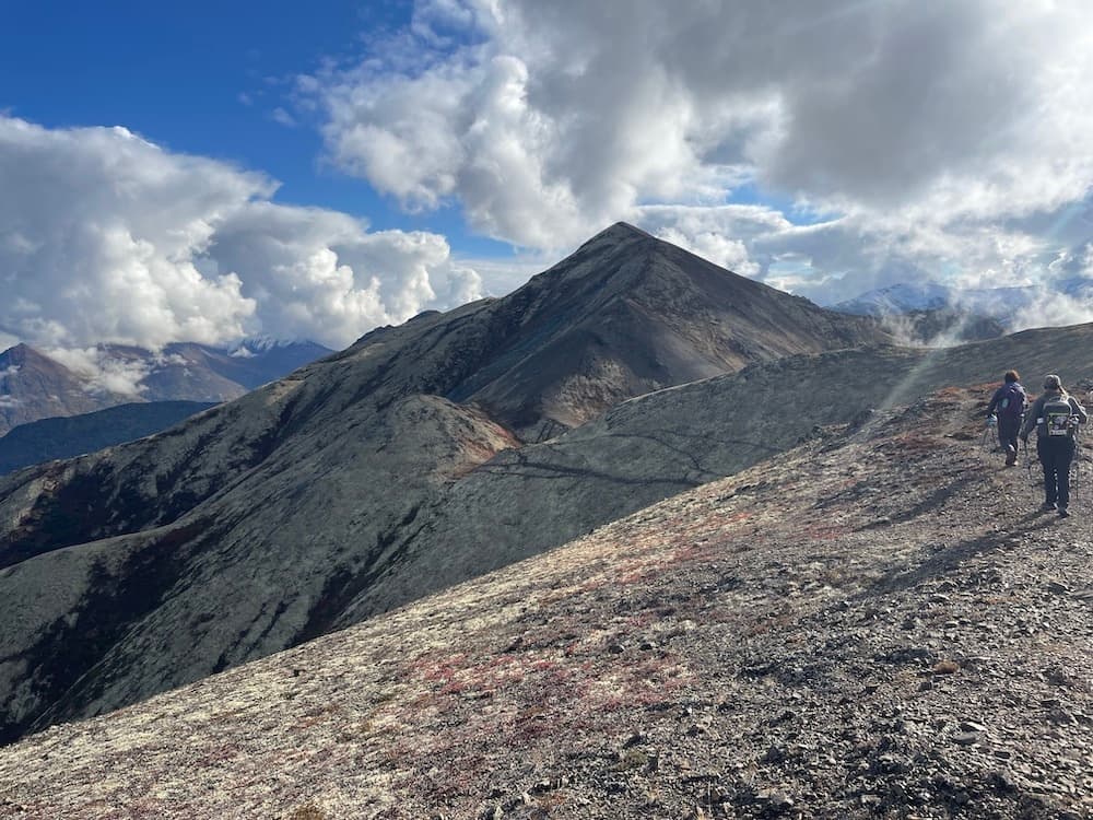 Hikers traversing exposed mountain ridge under dramatic clouds