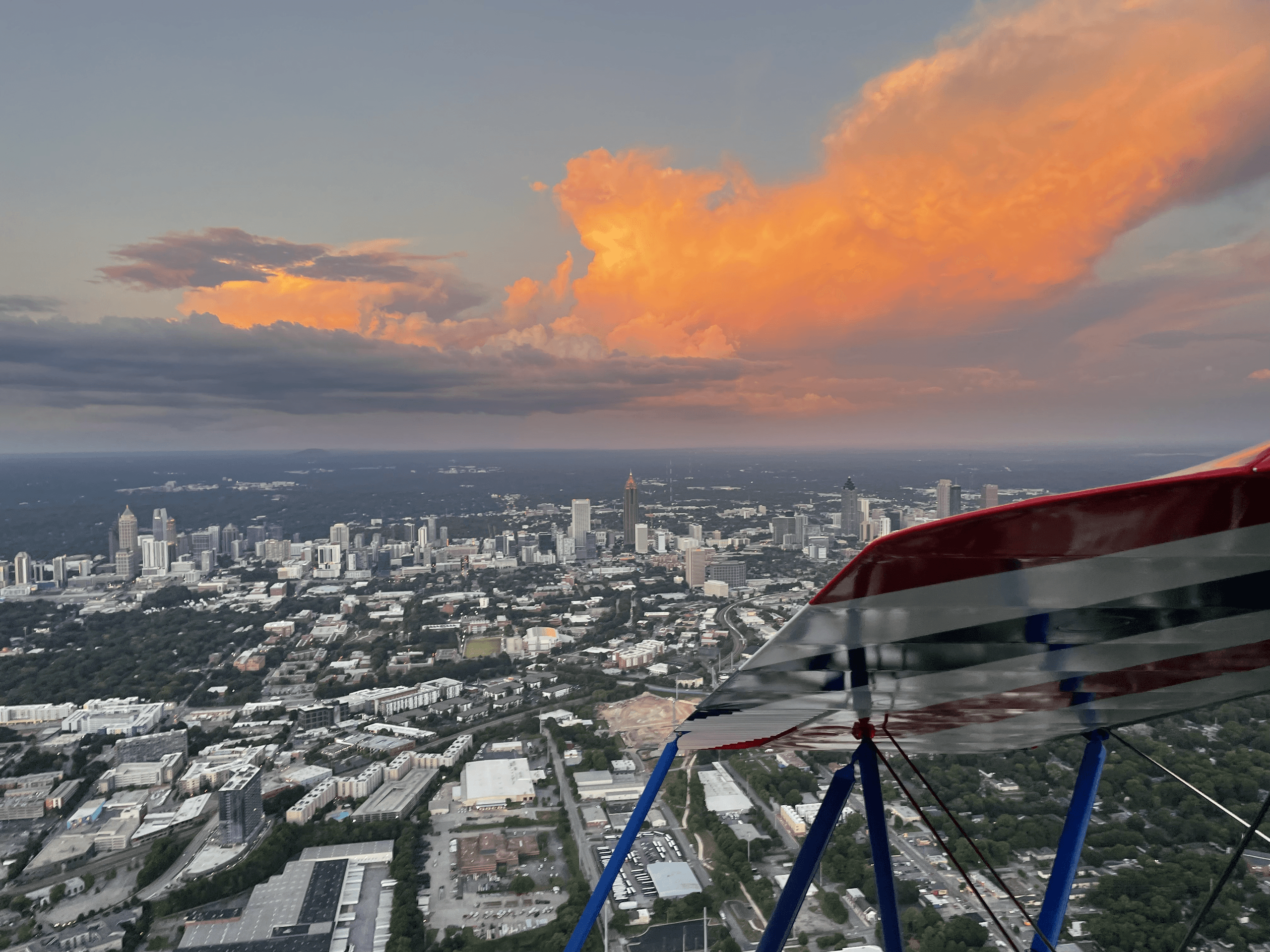 Biplane aerial over urban cityscape with dramatic sunset clouds
