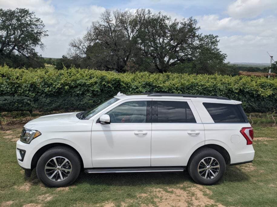 White SUV parked by vineyard beside oak trees on winery tour