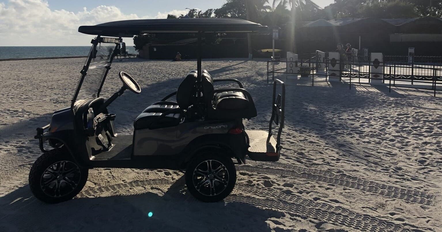 Golf cart parked on sandy beach at sunset, island rental ride