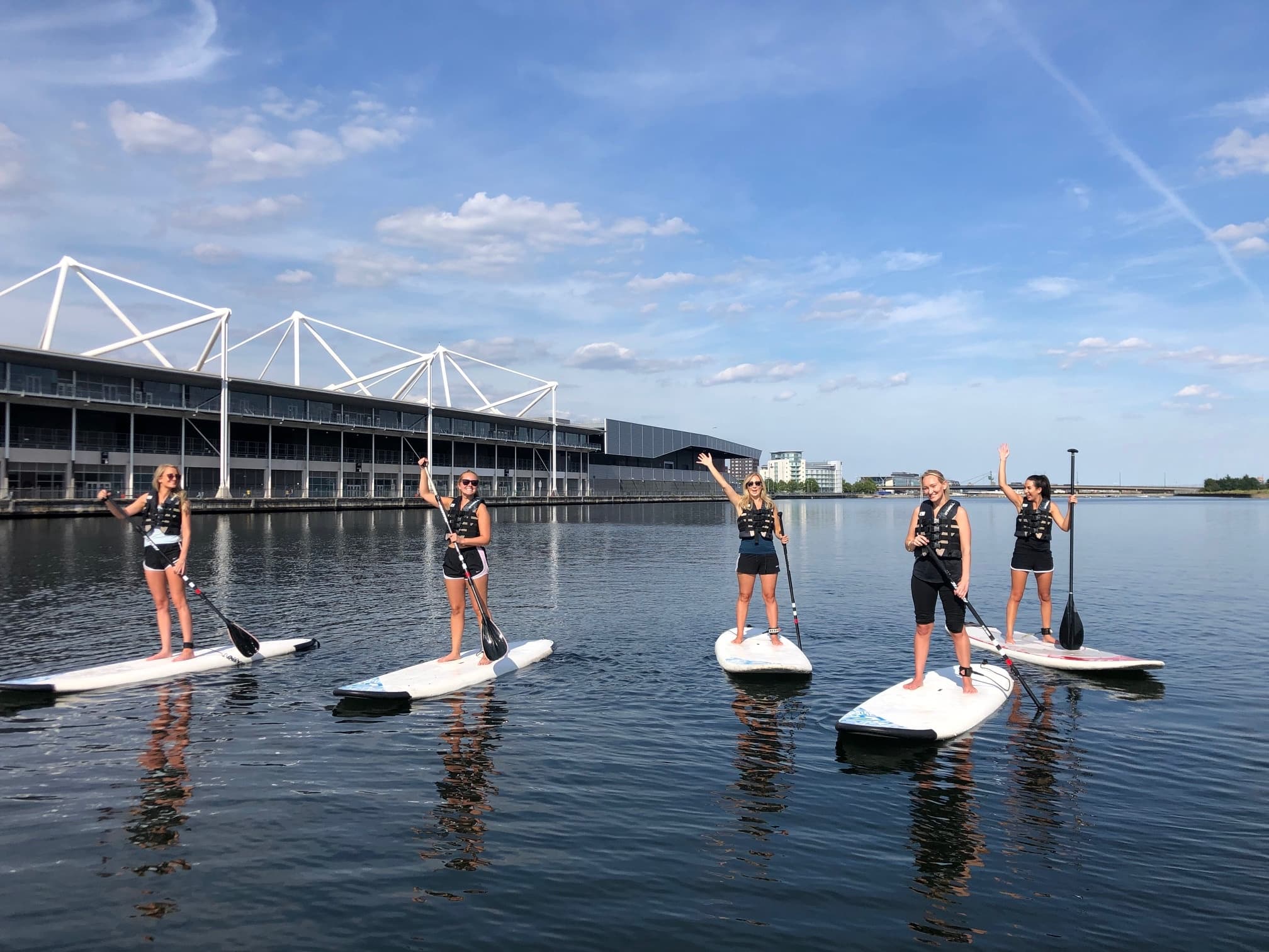 Group paddleboarding on calm docklands water with stadium backdrop