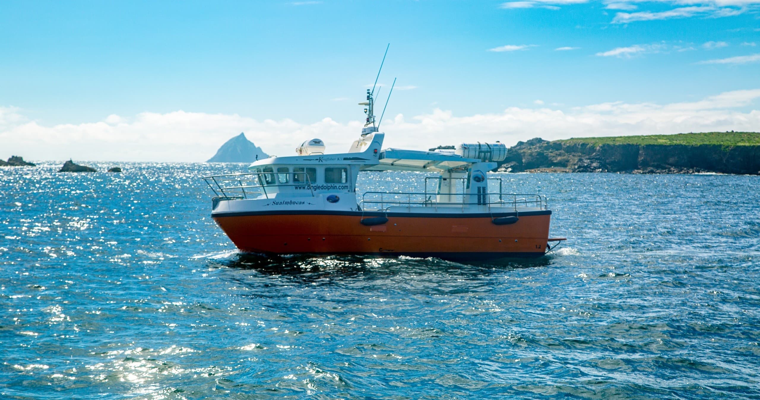 Passenger boat cruising sparkling open sea near rugged shore