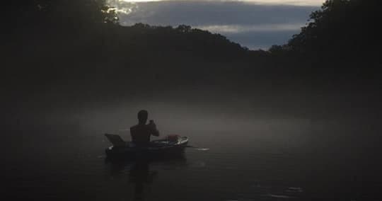 Solo kayaker paddling through misty mountain river at dawn