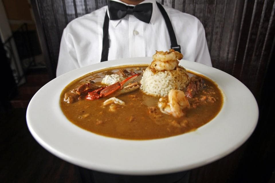 Server presenting gumbo bowl with rice, classic New Orleans dining