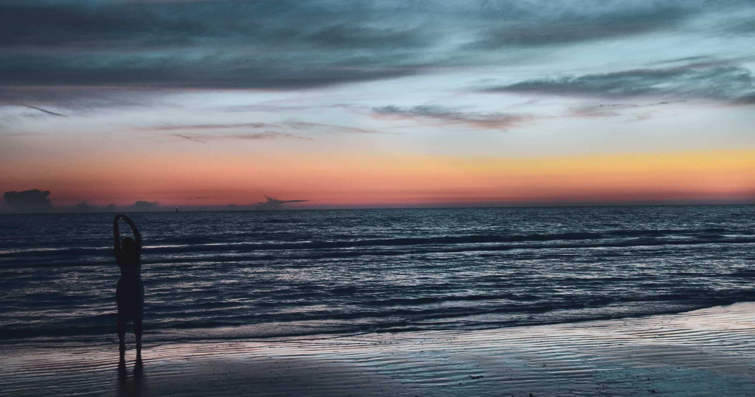 Person standing on beach at sunset enjoying ocean view