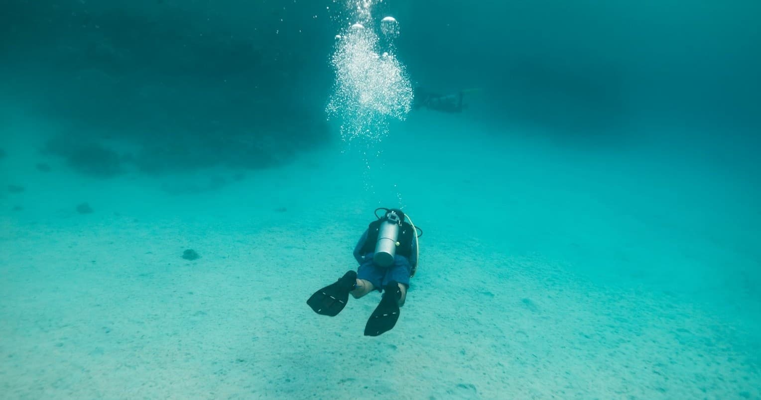 Solo diver descending into clear shallow turquoise sea