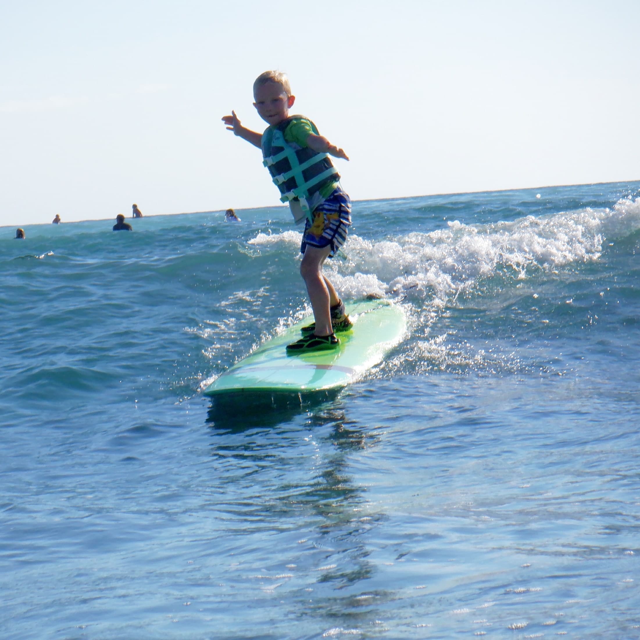 Child surfing small wave in ocean wearing life vest near shore