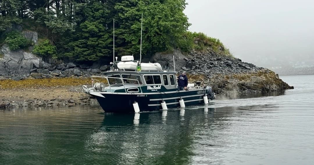 Expedition boat cruising calm rocky forested shoreline, coastal landing
