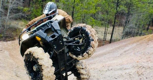 ATV performing wheelie on muddy forest trail, adrenaline ride