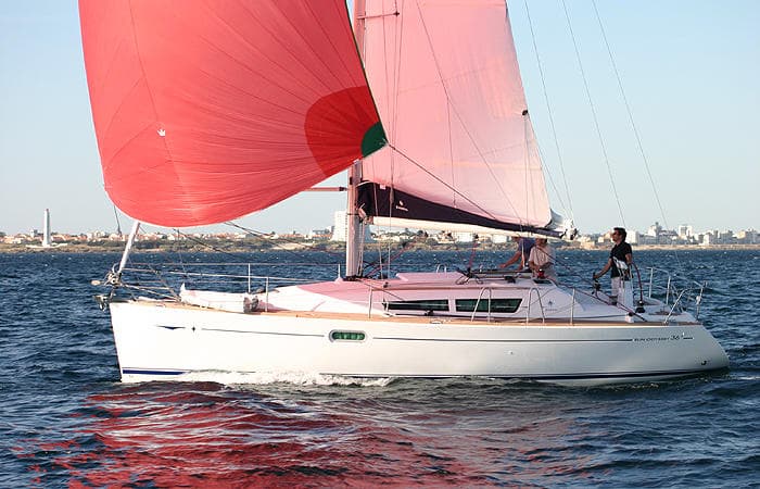 Sailboat flying red spinnaker on sparkling sea, coastal skyline