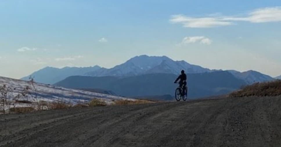 Cyclist silhouetted on mountain ridge riding toward peaks