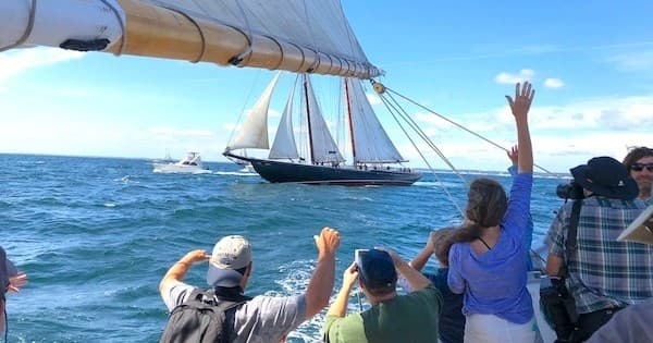 Passengers waving aboard a coastal sailboat watching a schooner