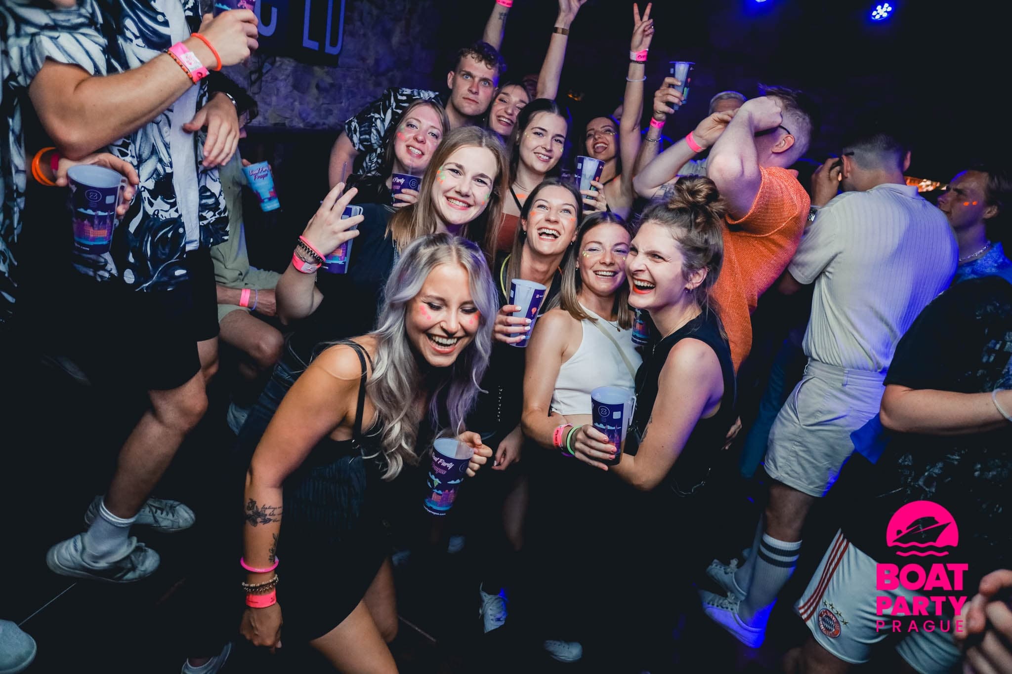 Large nightclub crowd dancing indoors with drinks and lights
