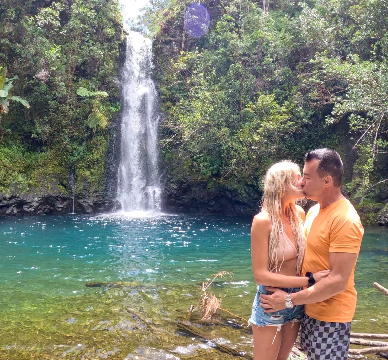 Couple embracing by turquoise waterfall pool in lush jungle