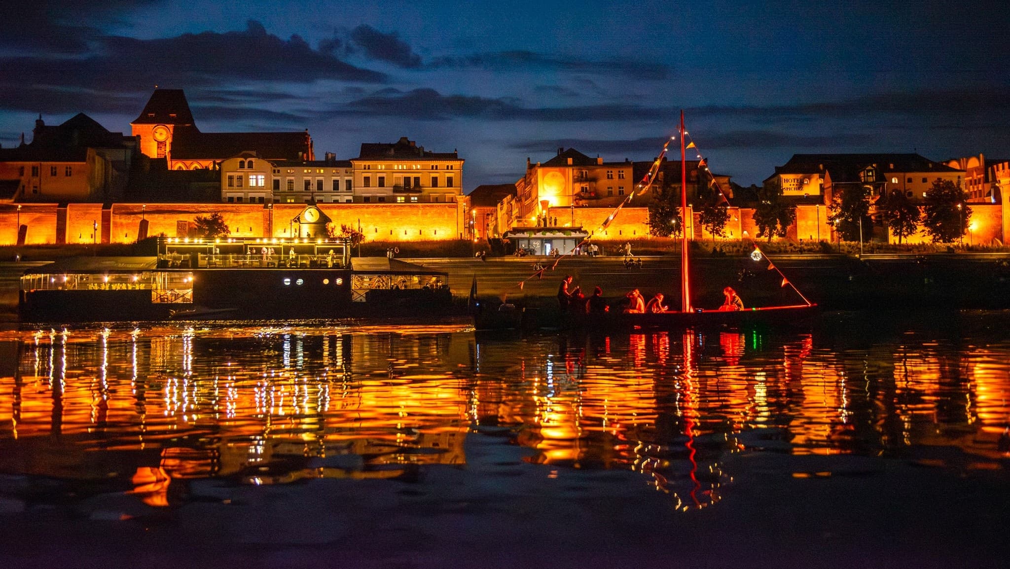 Nighttime riverfront town with illuminated boats and reflections
