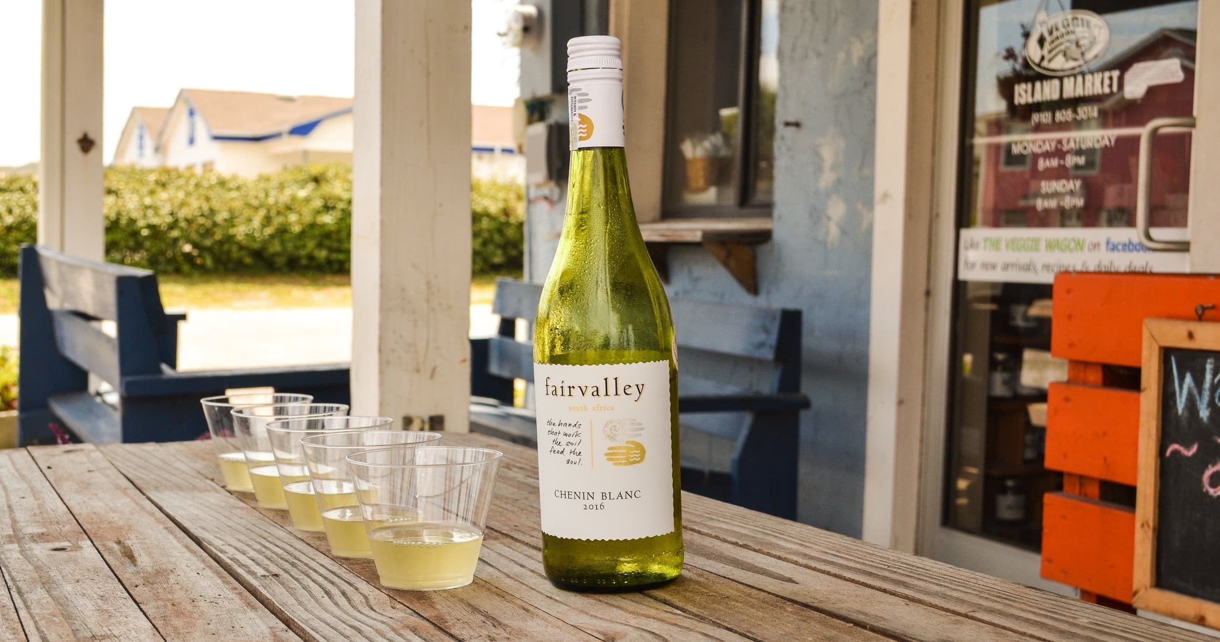 Outdoor wine tasting with bottle and sample cups on wooden table