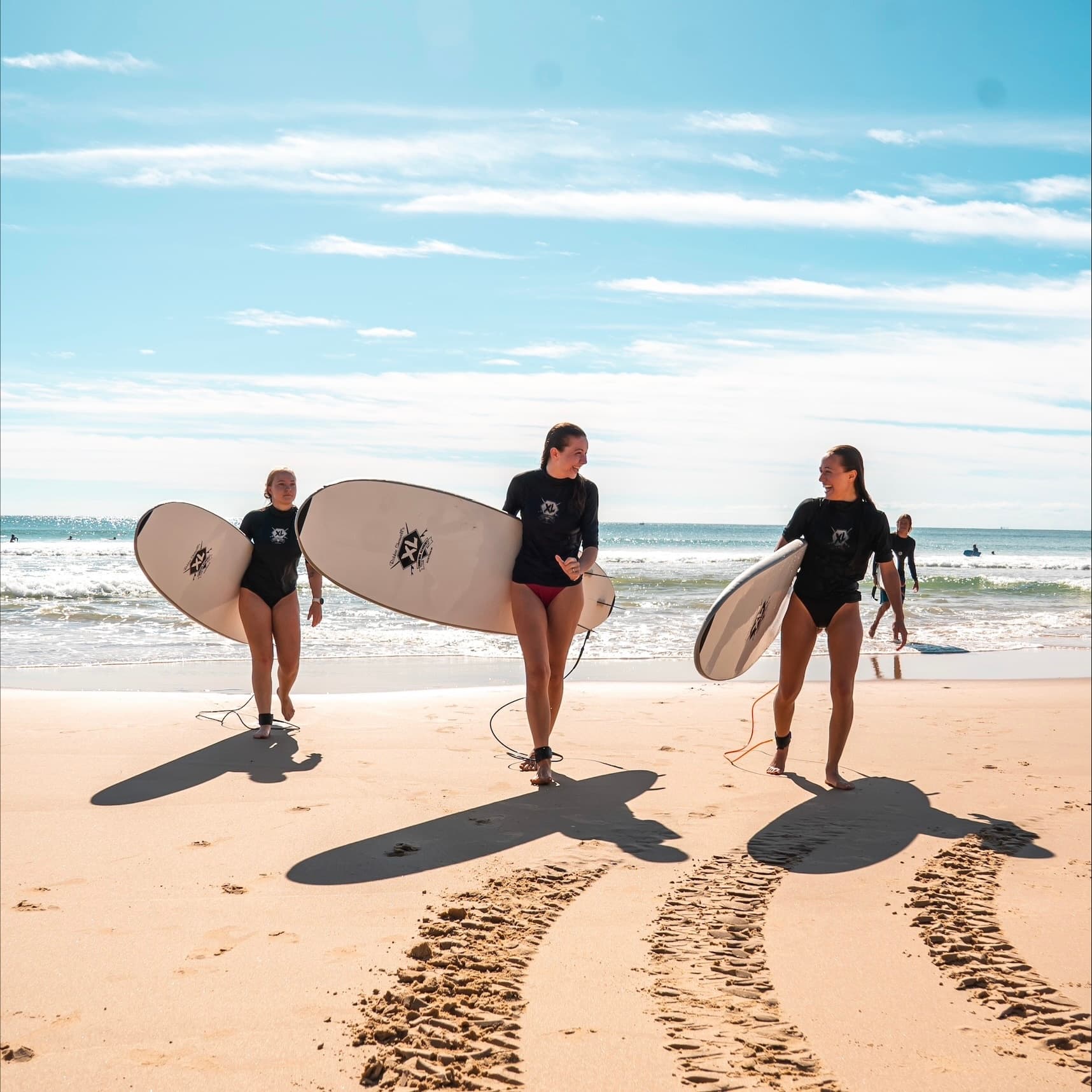 Three surfers walking on sunny beach with boards leaving tracks