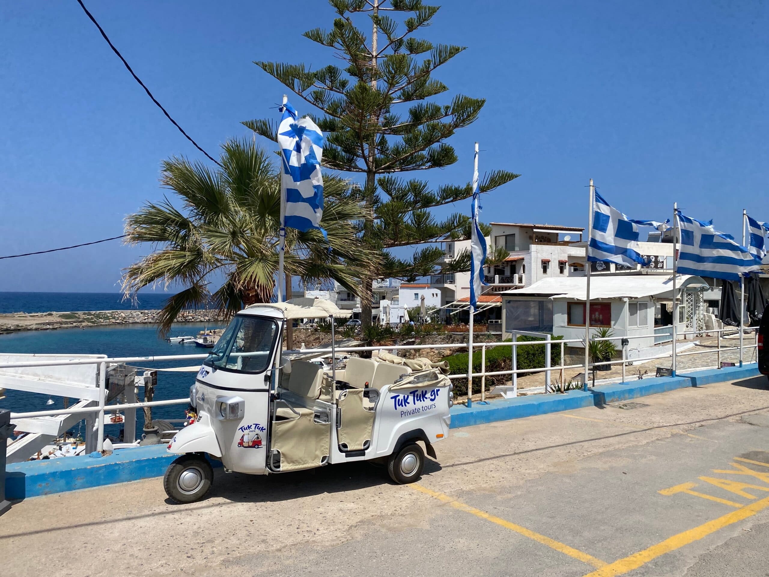 Tuk-tuk parked by seaside with Greek flags on coastal road