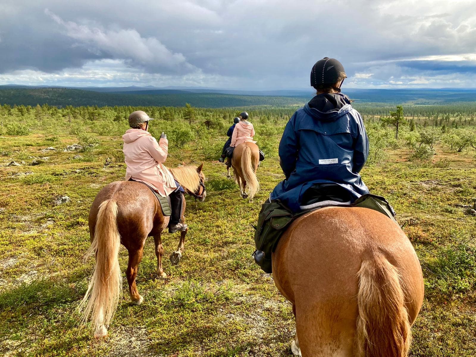 Group horseback riding across open tundra with stormy sky