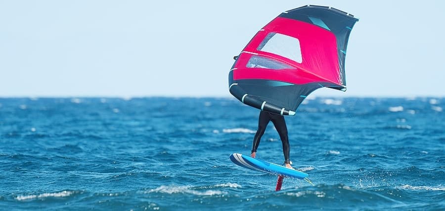 Wing foiler gliding over open ocean with pink wing in action