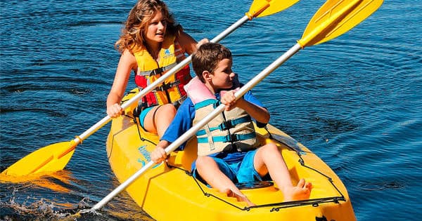 Two kids kayaking in yellow tandem kayak on calm blue water