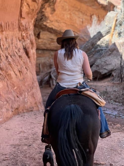 Back view of rider on horseback riding through narrow red rock canyon trail