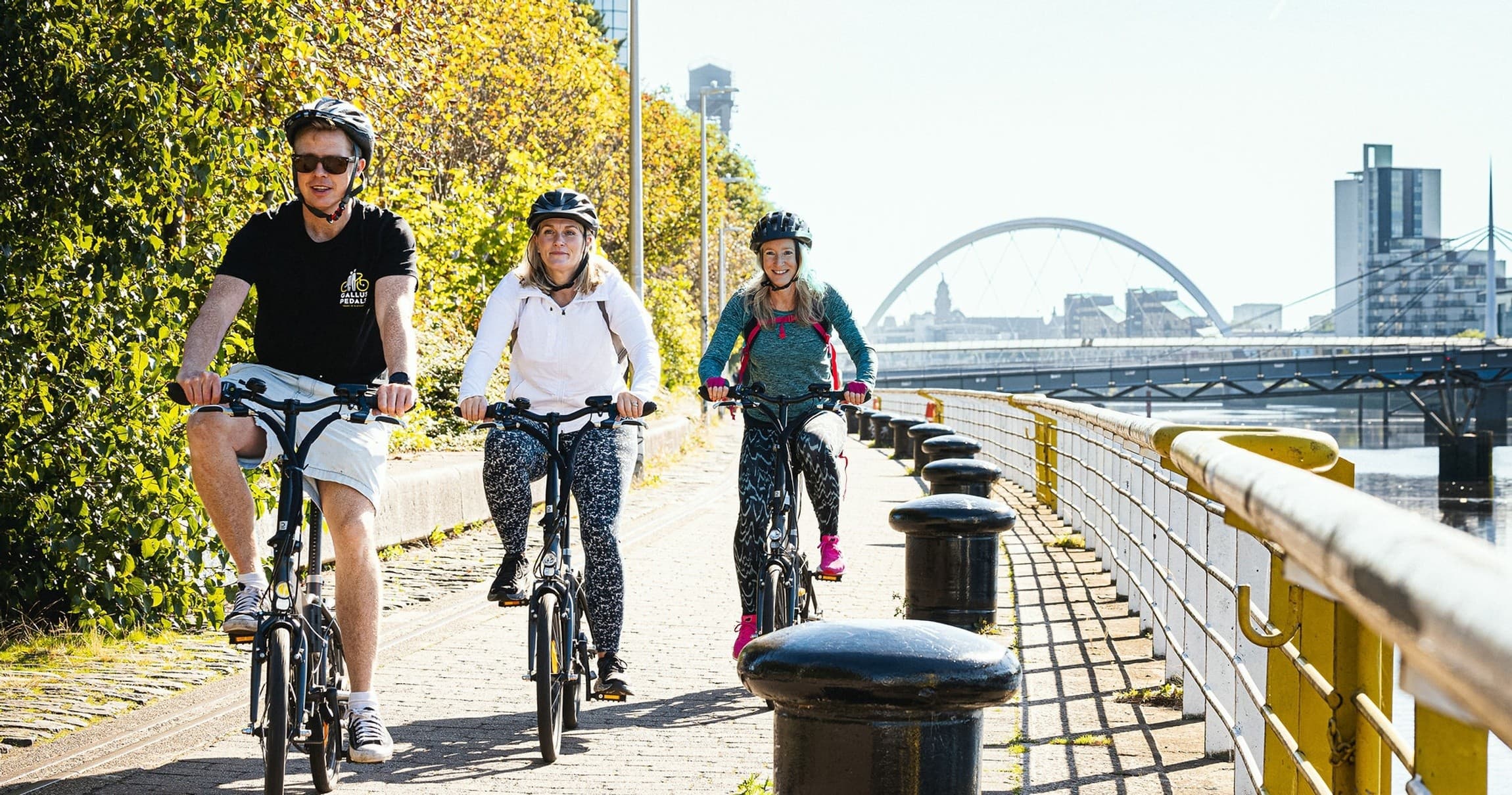 Cyclists riding riverside path with city bridge skyline