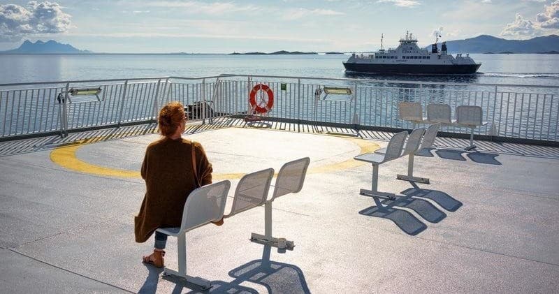 Passenger sitting on ferry deck watching open sea and distant ship