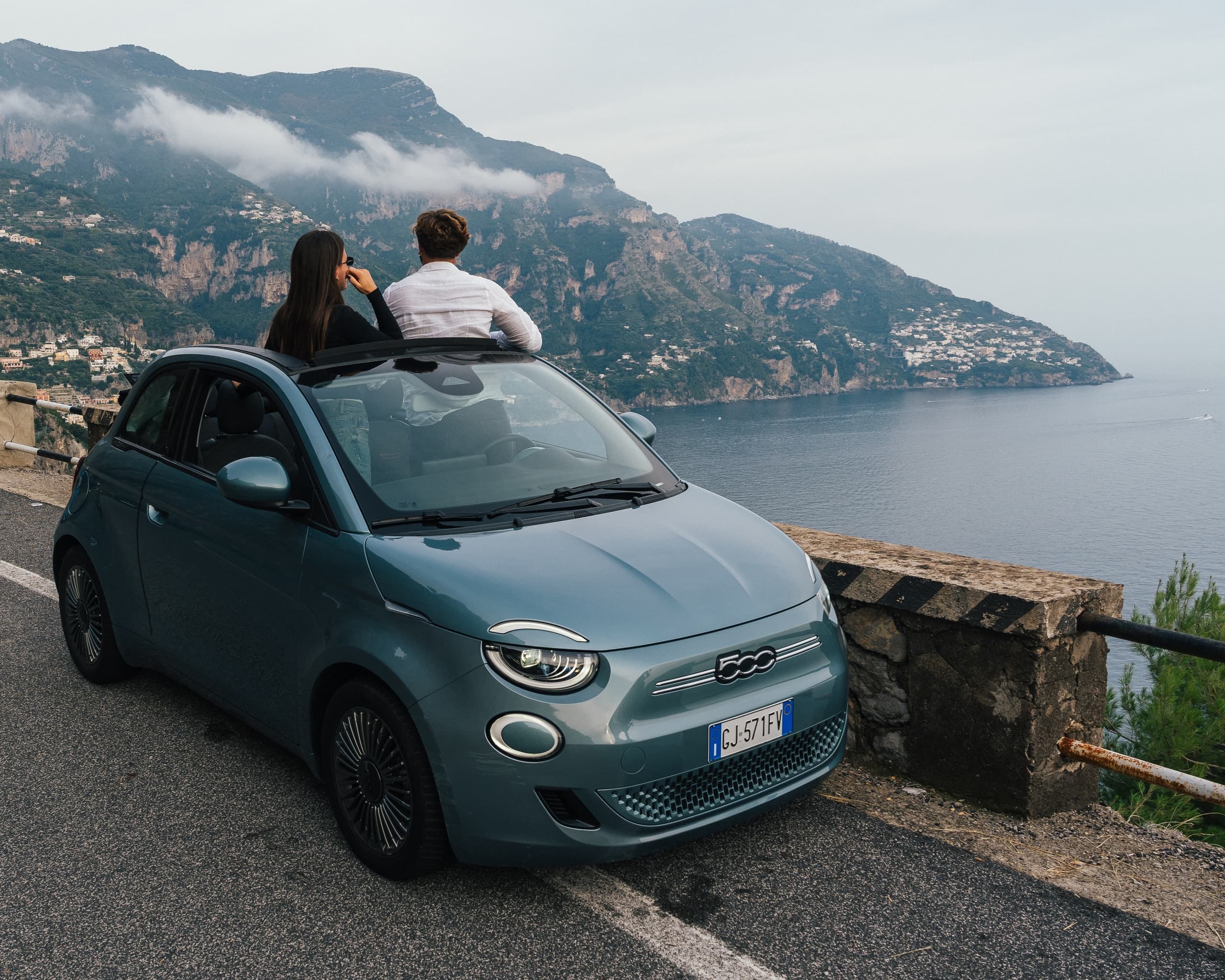 Couple on small car rooftop enjoying coastal overlook at Amalfi Coast